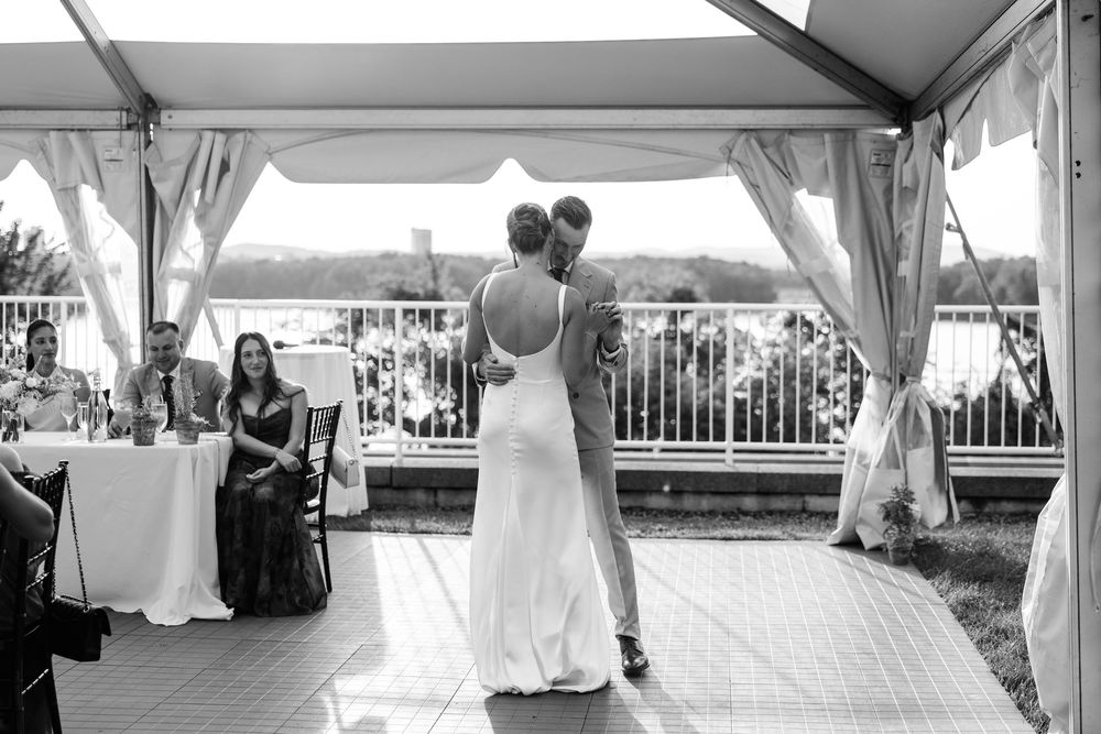 Black and white photo of a couple sharing their first dance at an outdoor wedding reception under a tent.