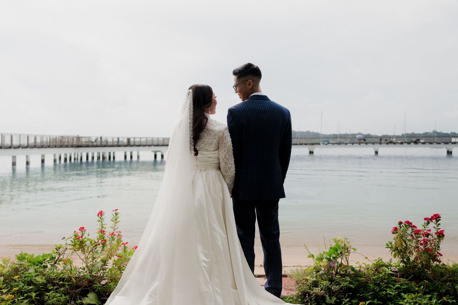 A bride and groom stand together overlooking a serene waterway on their wedding day.