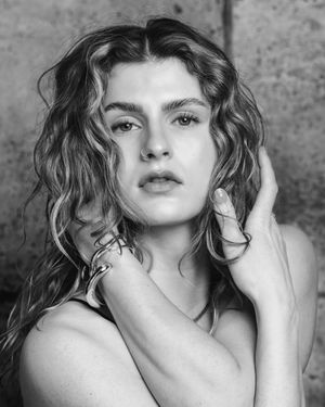 Black and white close-up portrait of a woman with wet curly hair, hand near face, intense gaze.