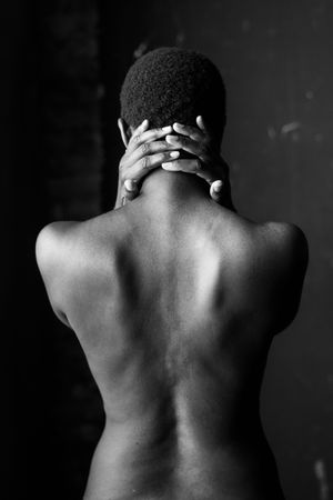 Black and white photo of a person viewed from behind with hands clasped behind their neck.