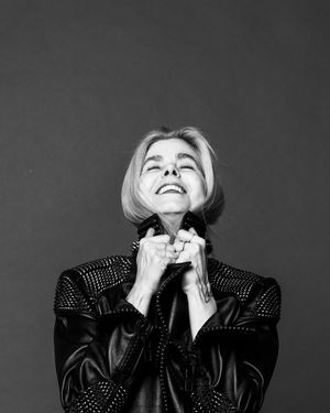 Black and white photo of an older woman in a studded leather jacket smiling and looking upward.