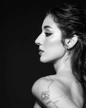 Black and white profile portrait of a woman with a rose tattoo on her shoulder against a dark background.