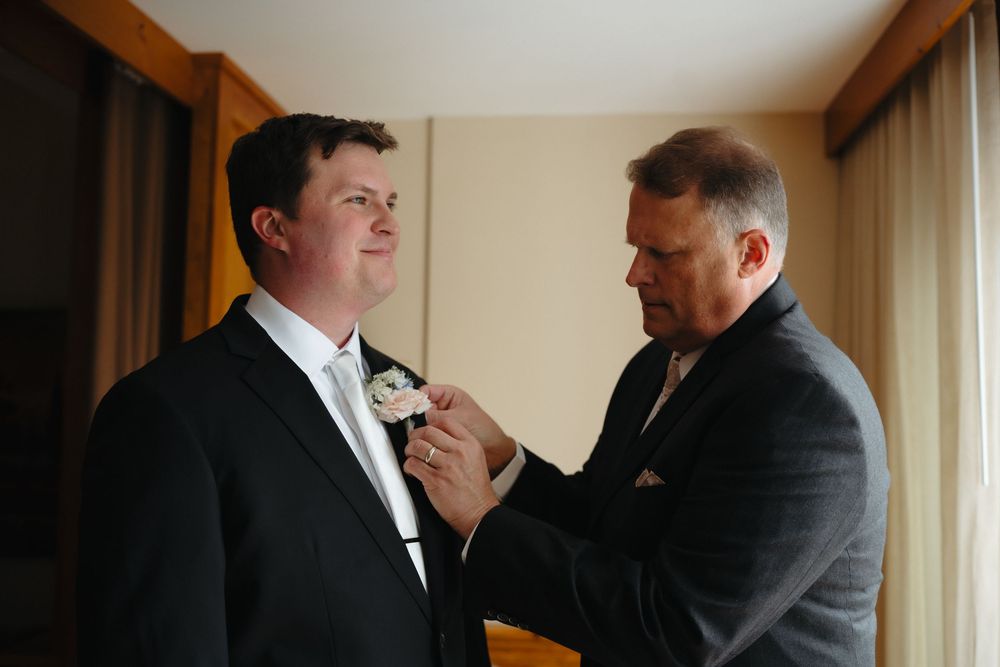 An older man pins a boutonniere on a groom's lapel before a wedding ceremony.