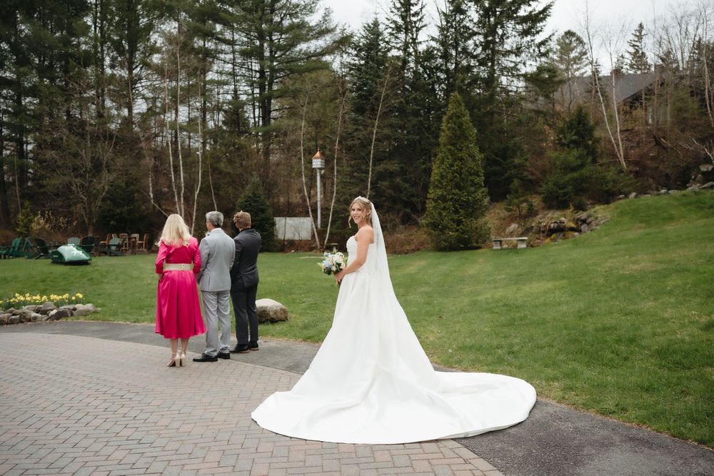Bride in a long white gown with cathedral veil standing on a garden path with guests.