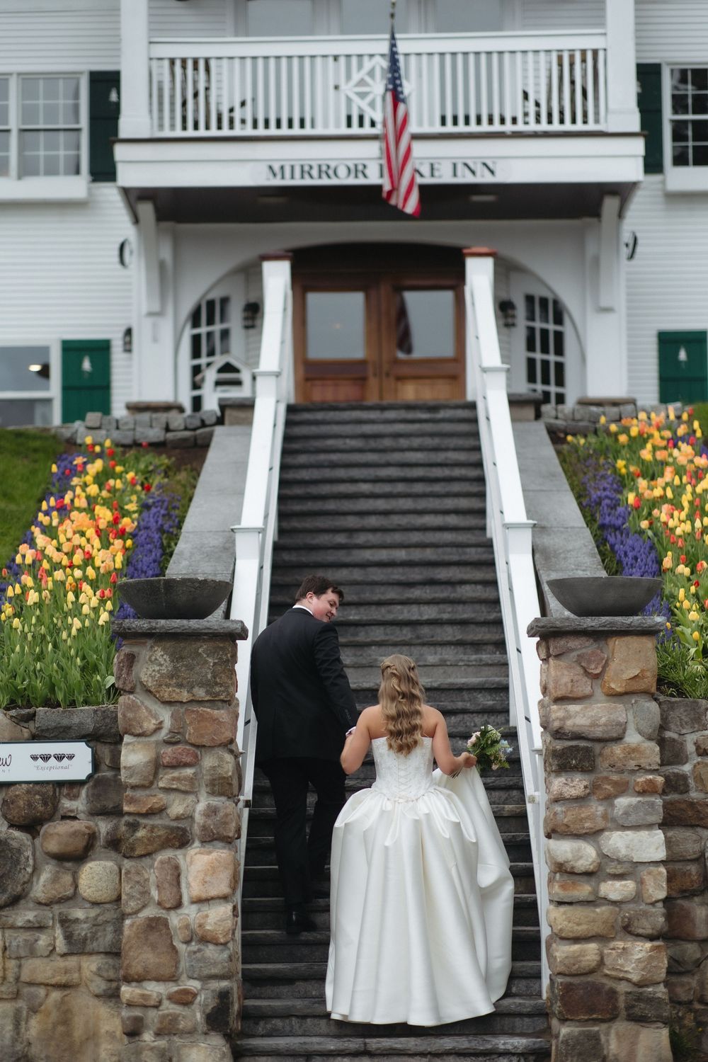 A bride and groom walk up stone steps toward the Mirror Lake Inn entrance.