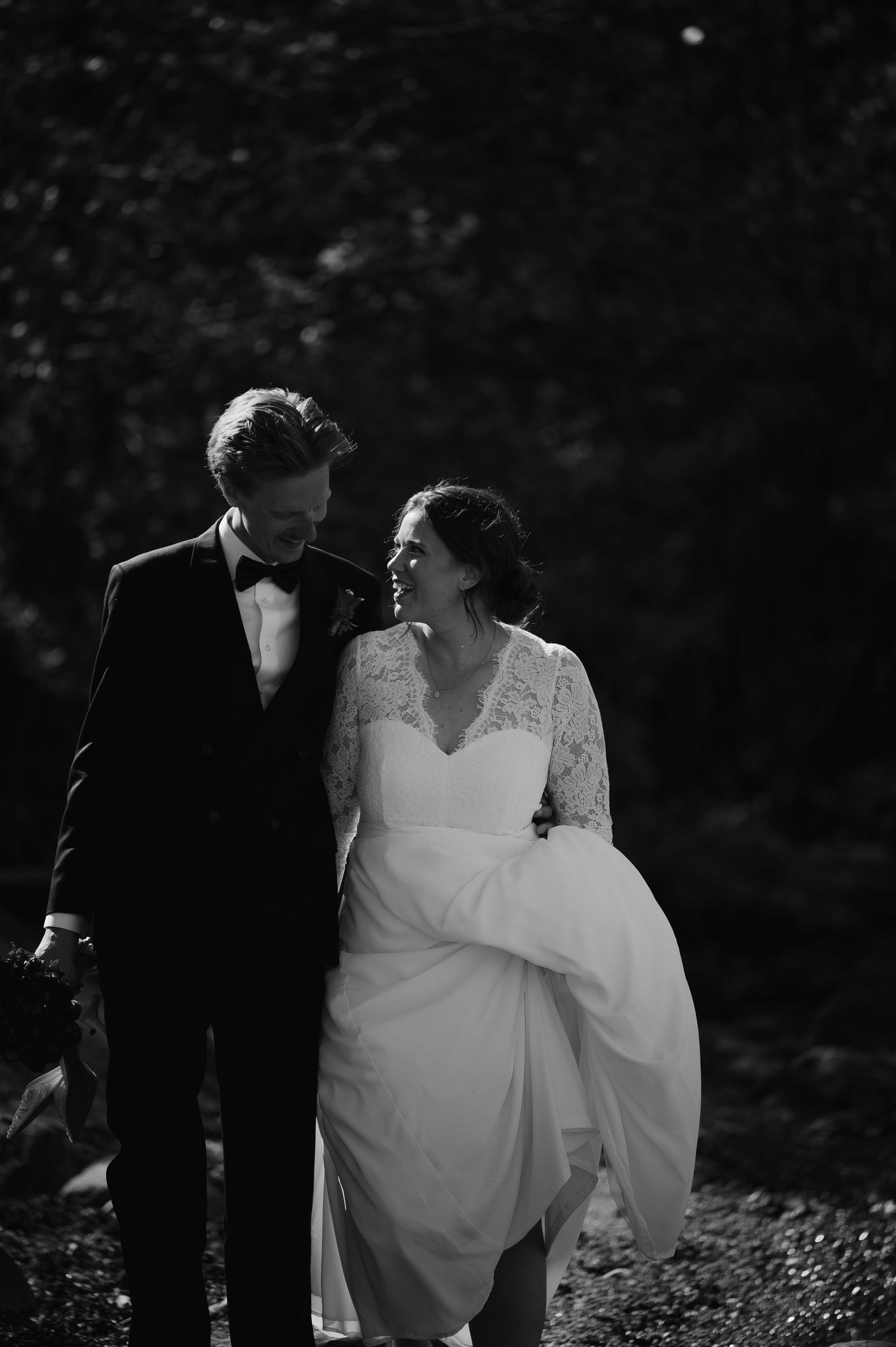 Black and white photo of a smiling bride and groom walking together outdoors on their wedding day.