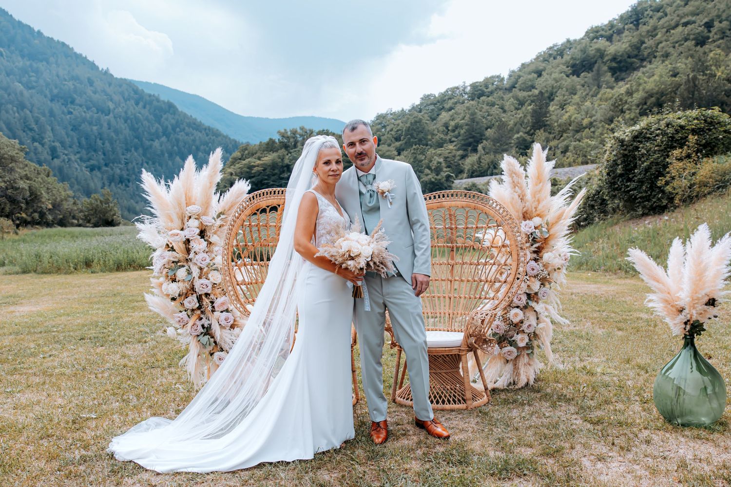 Bride and groom kissing at outdoor wedding altar with pampas grass decor and mountain backdrop.