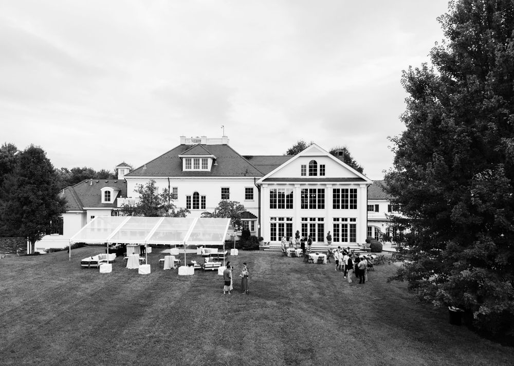 Black and white aerial view of a large white estate venue with outdoor event setup on manicured lawn.
