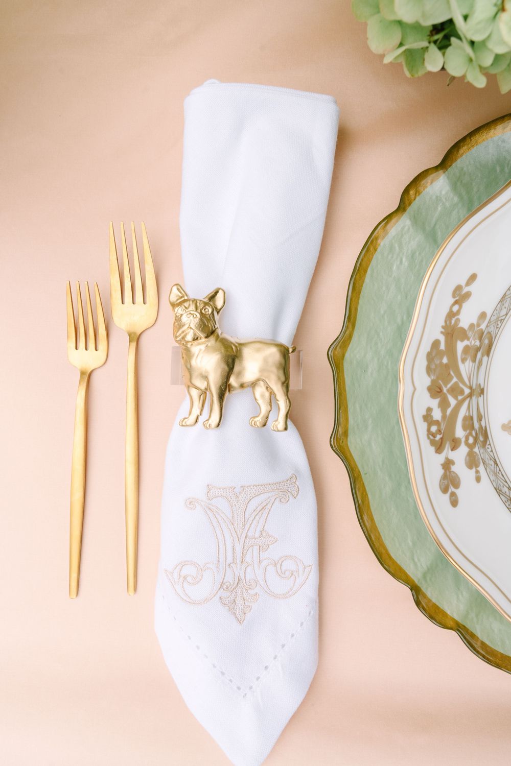 Gold French bulldog napkin ring on monogrammed white napkin with gold flatware and green charger plate.
