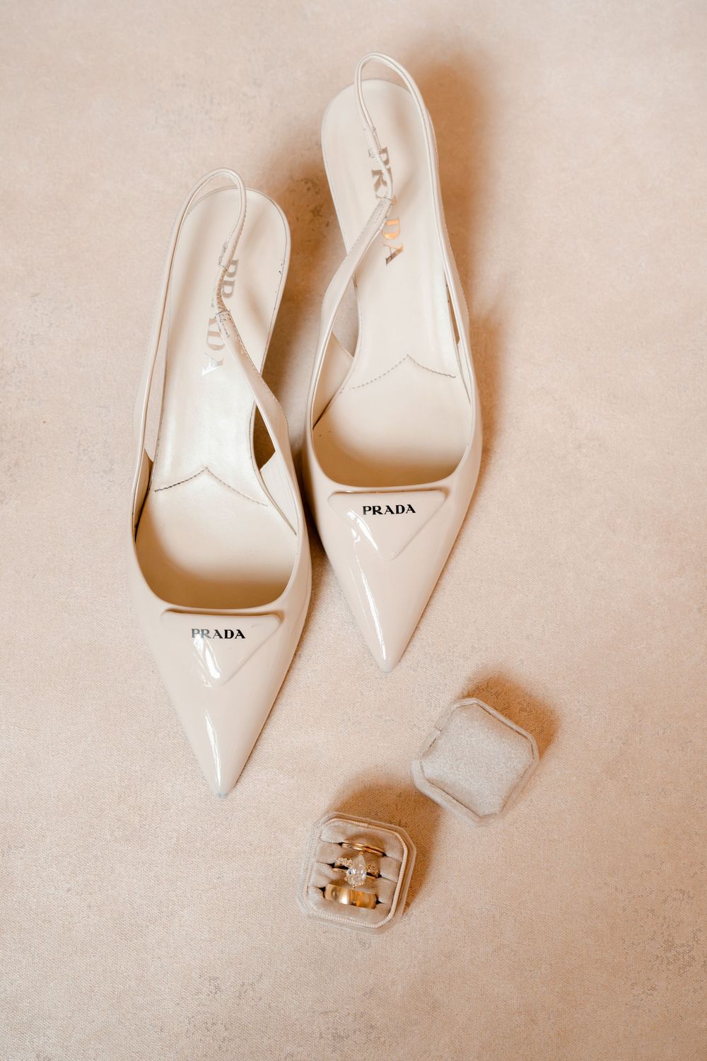 Prada ivory patent leather slingback heels displayed beside a velvet ring box with gold wedding bands.