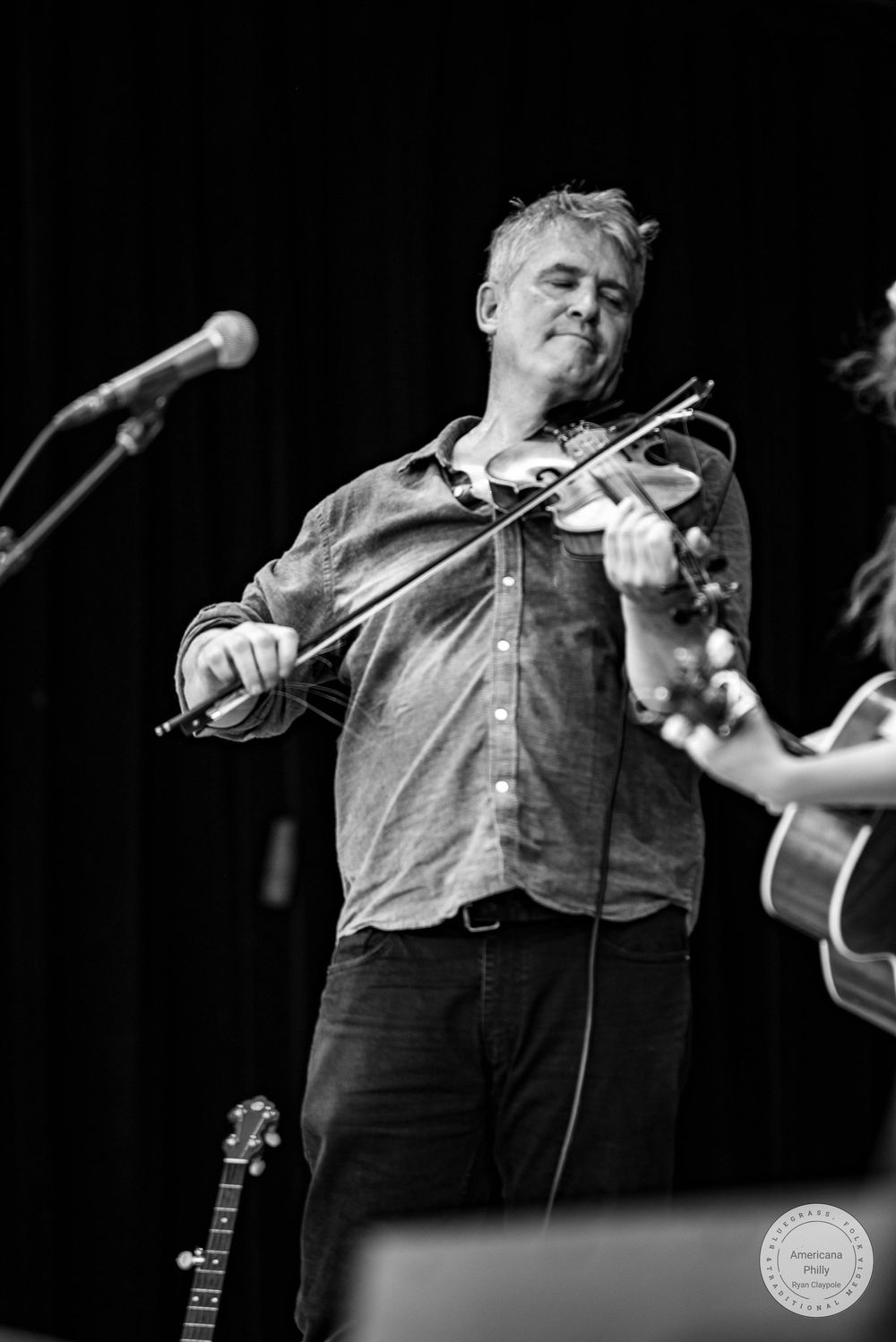 Black and white photo of a man passionately playing violin on stage with a microphone nearby.