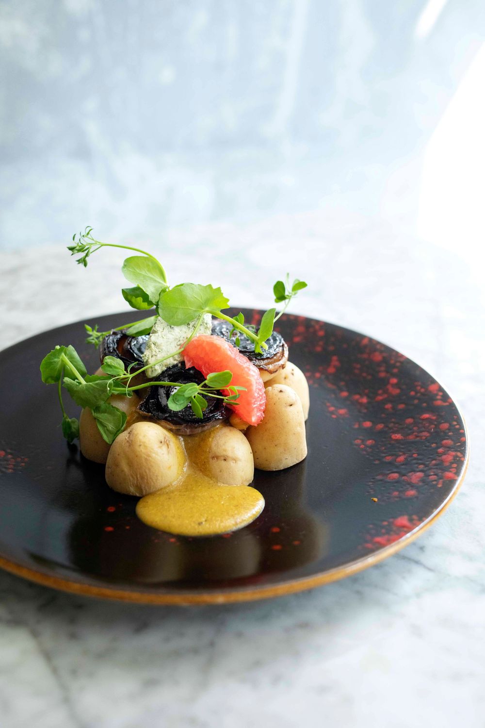 Elegant fine dining dish with baby potatoes, strawberry, microgreens, and sauce on a black plate.