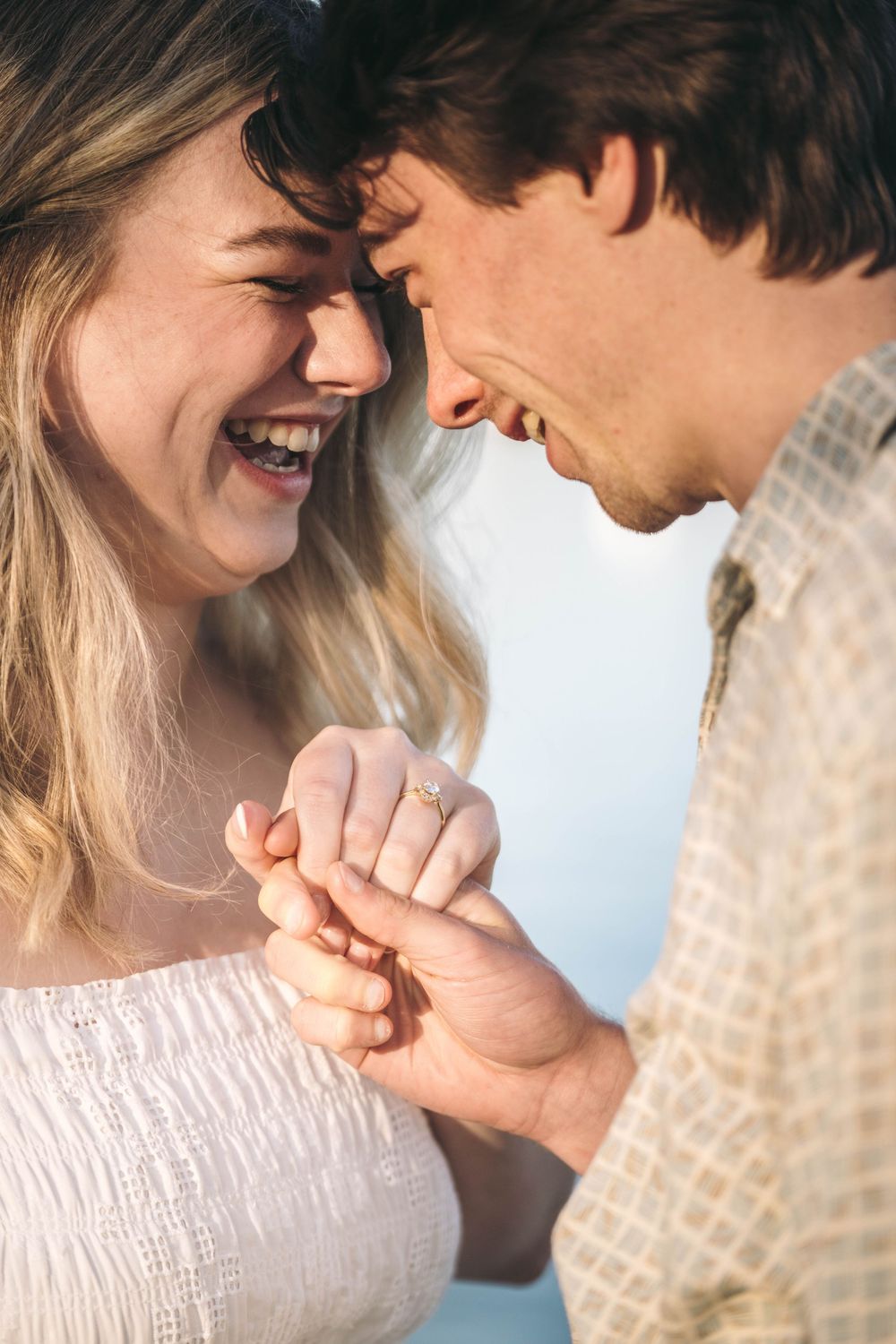 Joyful couple sharing an intimate moment, laughing together while showing off an engagement ring.