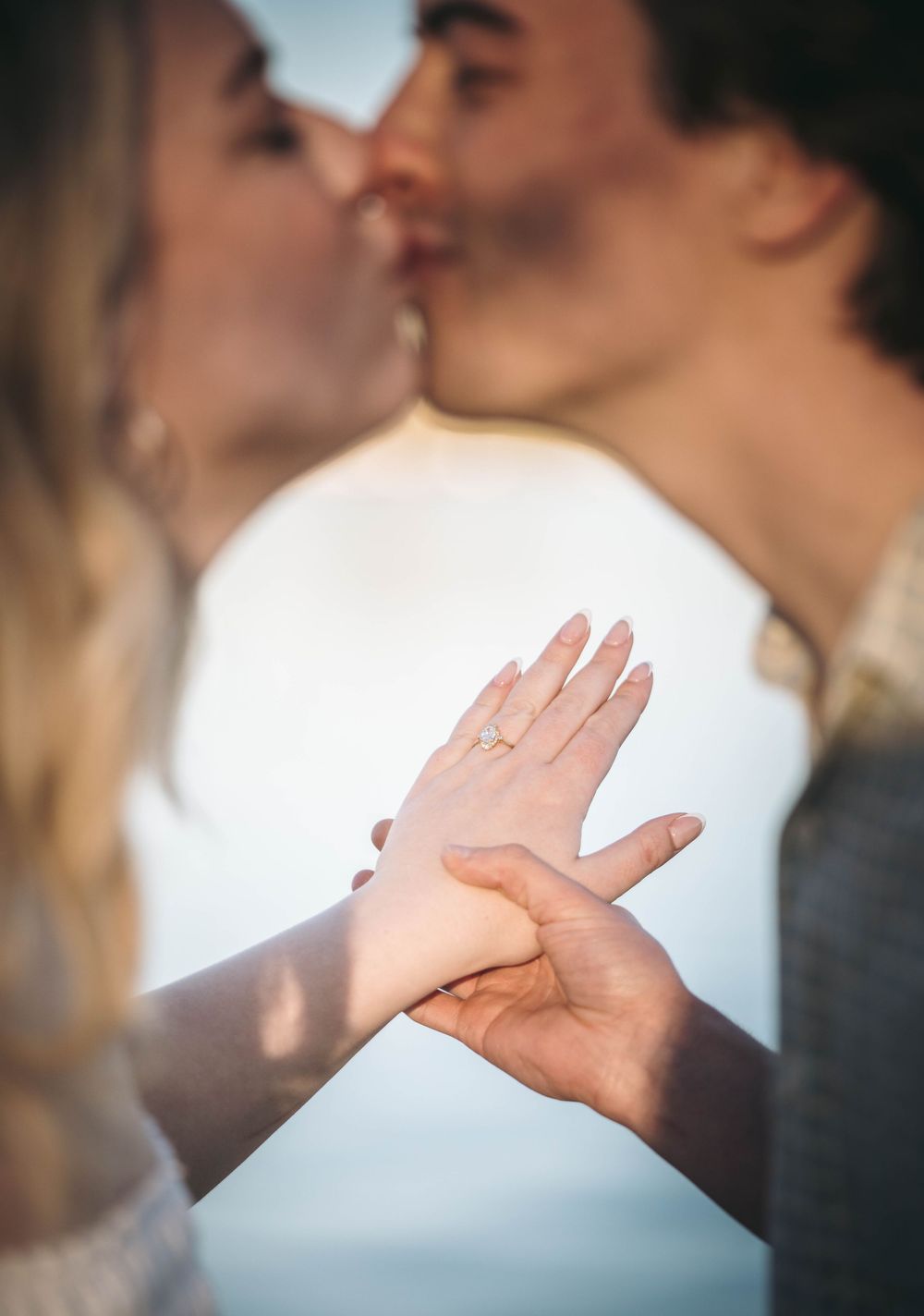 Couple kissing while showing off an engagement ring, celebrating their proposal with a romantic outdoor moment.