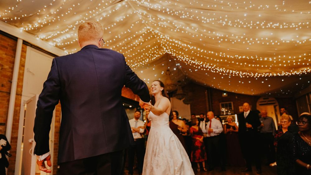 Bride and groom share first dance under twinkling fairy lights at elegant wedding reception venue.