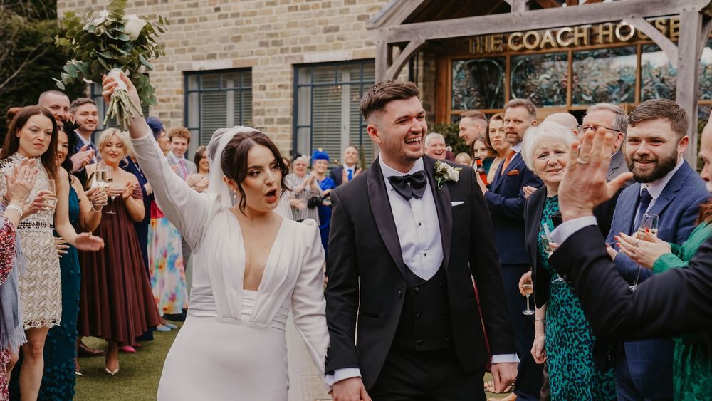 Joyful newlyweds celebrate with confetti outside The Coach House venue, surrounded by cheering wedding guests.
