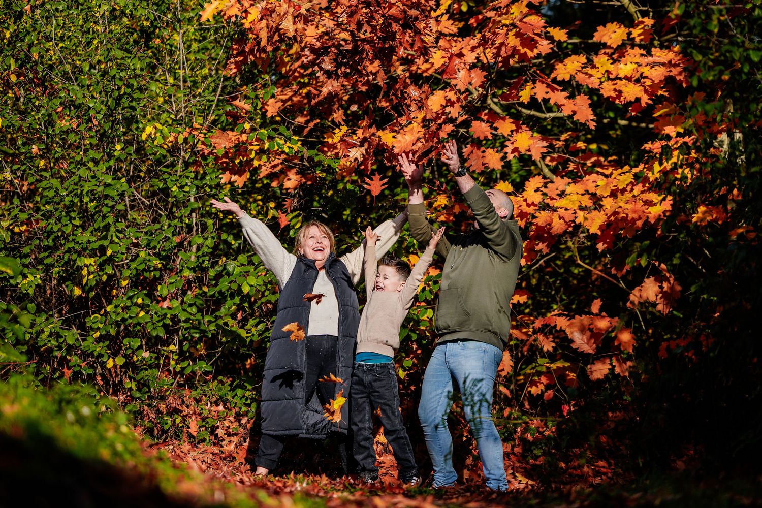 Three people joyfully tossing autumn leaves in a colorful fall forest setting.