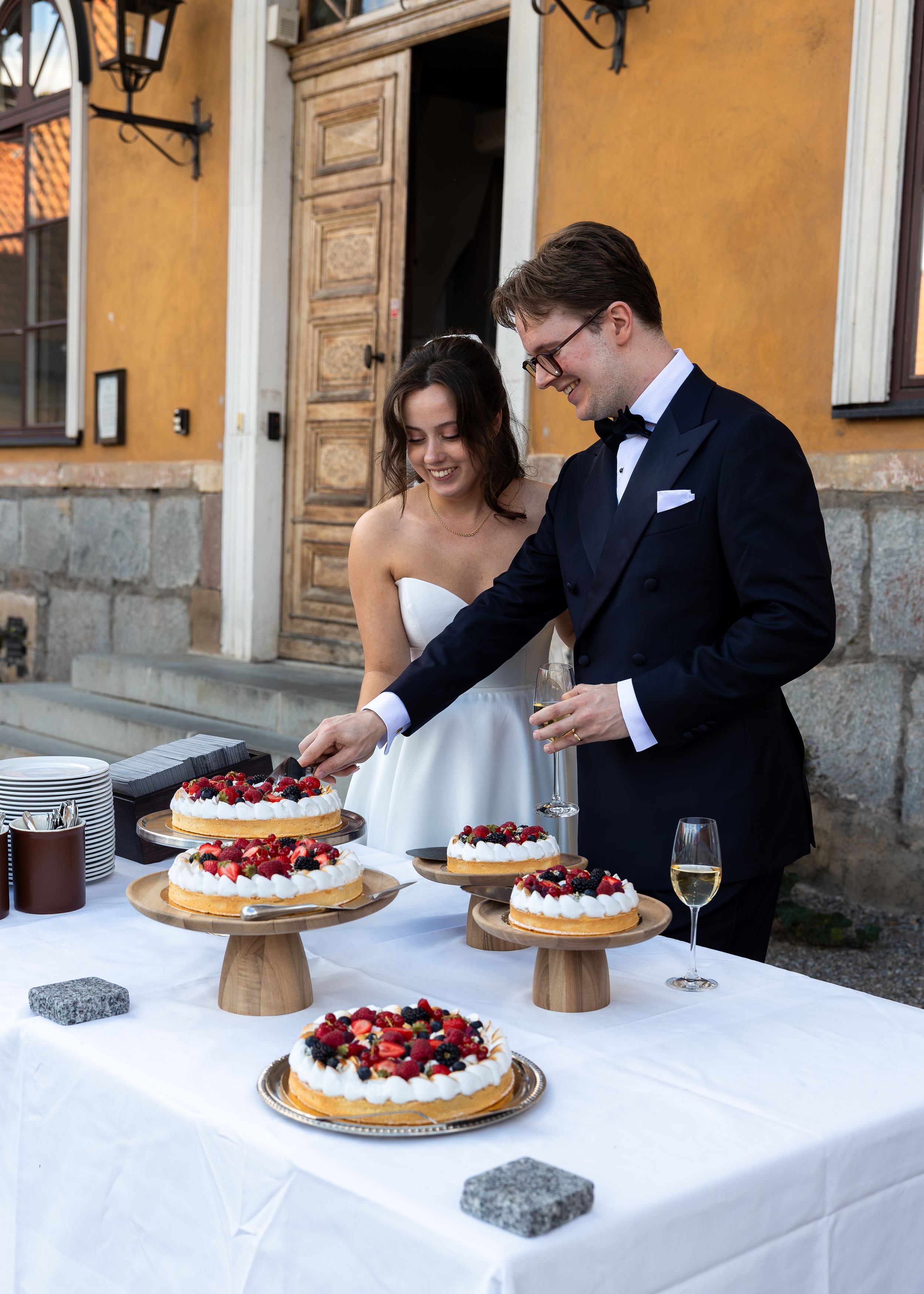 Brudpar skär tårta på Ulfsunda Slott, vackert par, sommartårta med jordgubbar. Bröllop på Ulfsunda slott. Bröllopsfotograf i Stockholm.