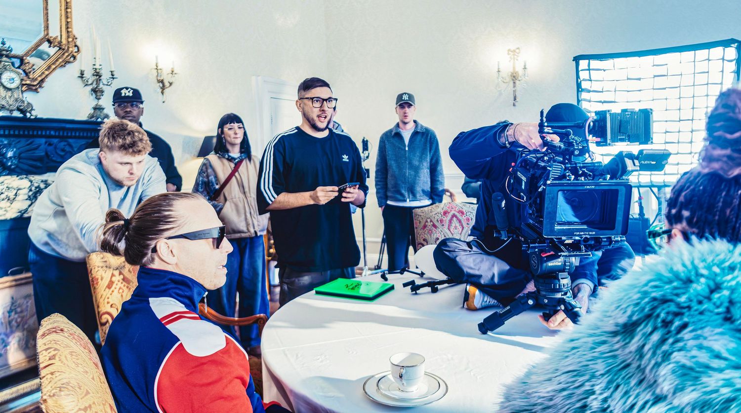 Behind-the-scenes film shoot with crew and camera equipment in an elegant room with ornate decor.