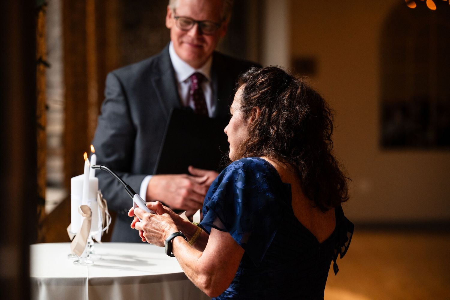 Wedding guest lighting unity candle during indoor wedding ceremony at elegant venue.
