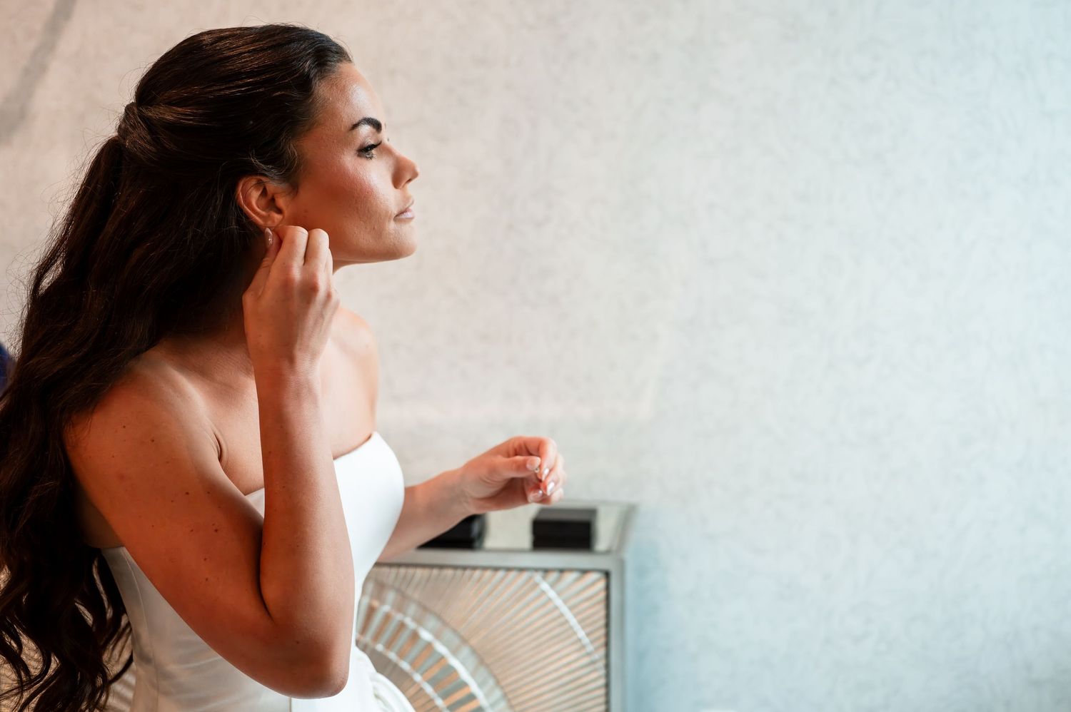 Young woman in white towel touching her ear, enjoying a serene spa moment with elegant long dark hair.