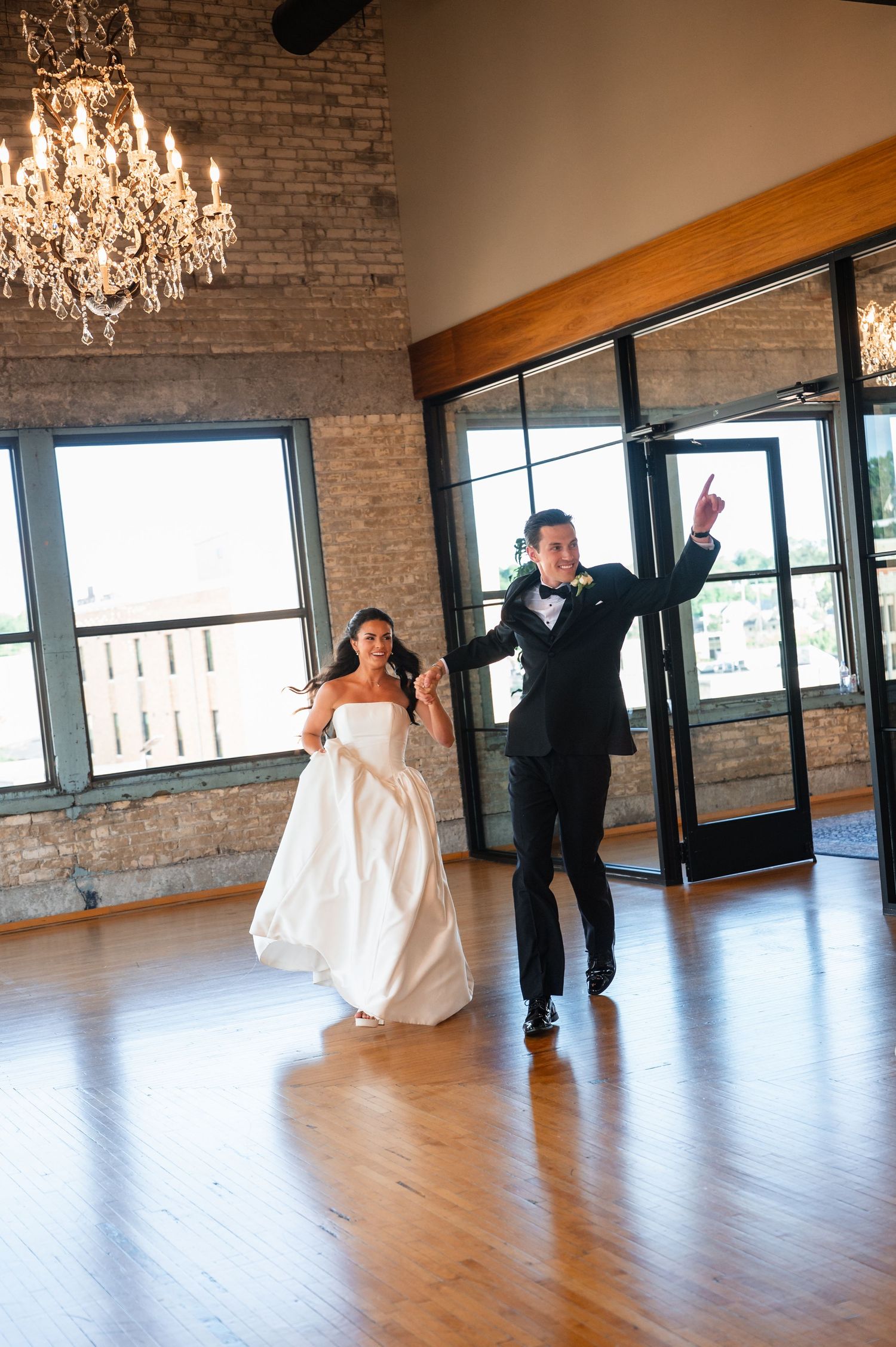 Bride and groom make a grand entrance into their rustic wedding reception venue with chandelier.