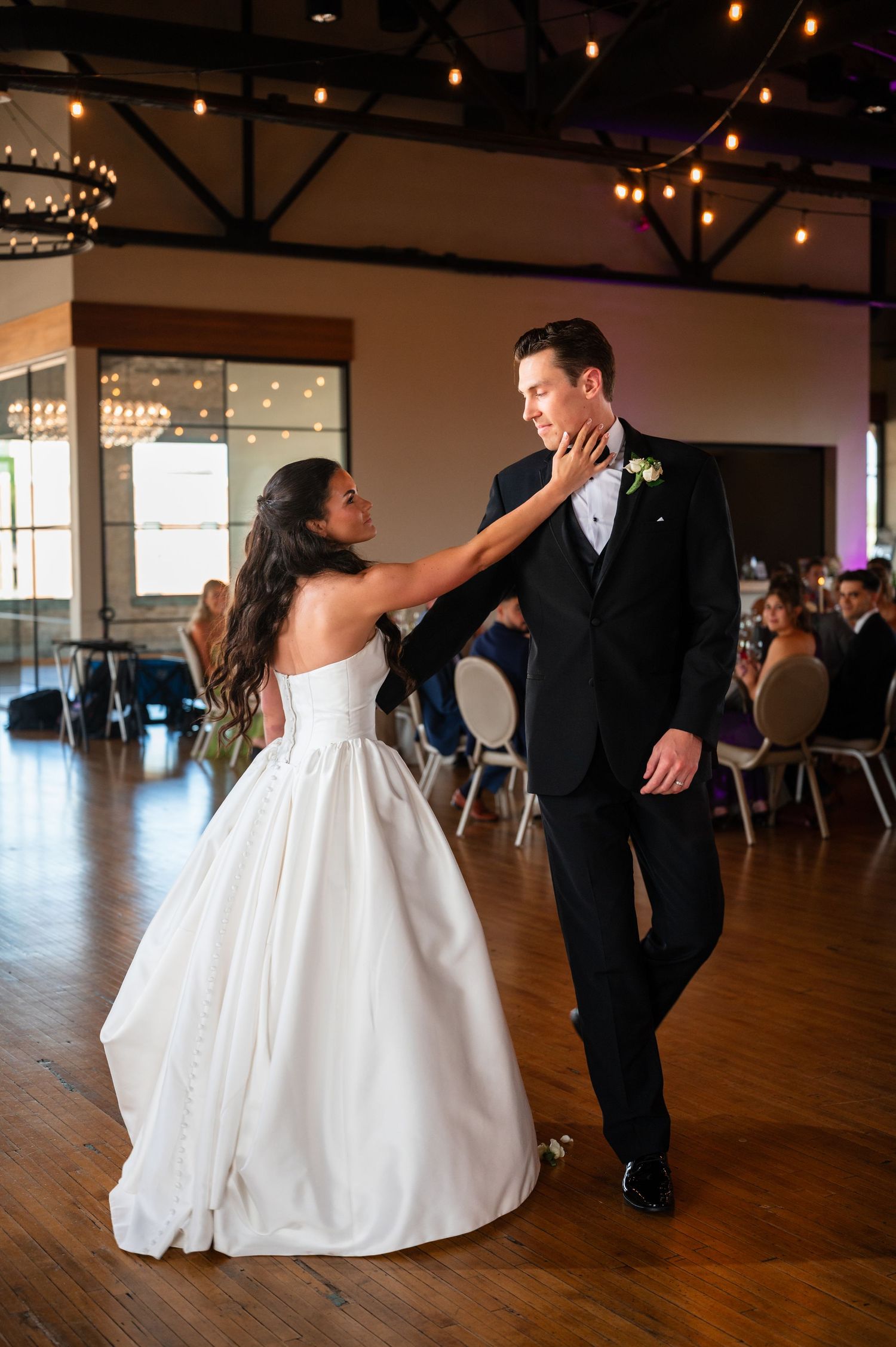 Bride and groom share their first dance on a wooden dance floor at a romantic wedding reception.