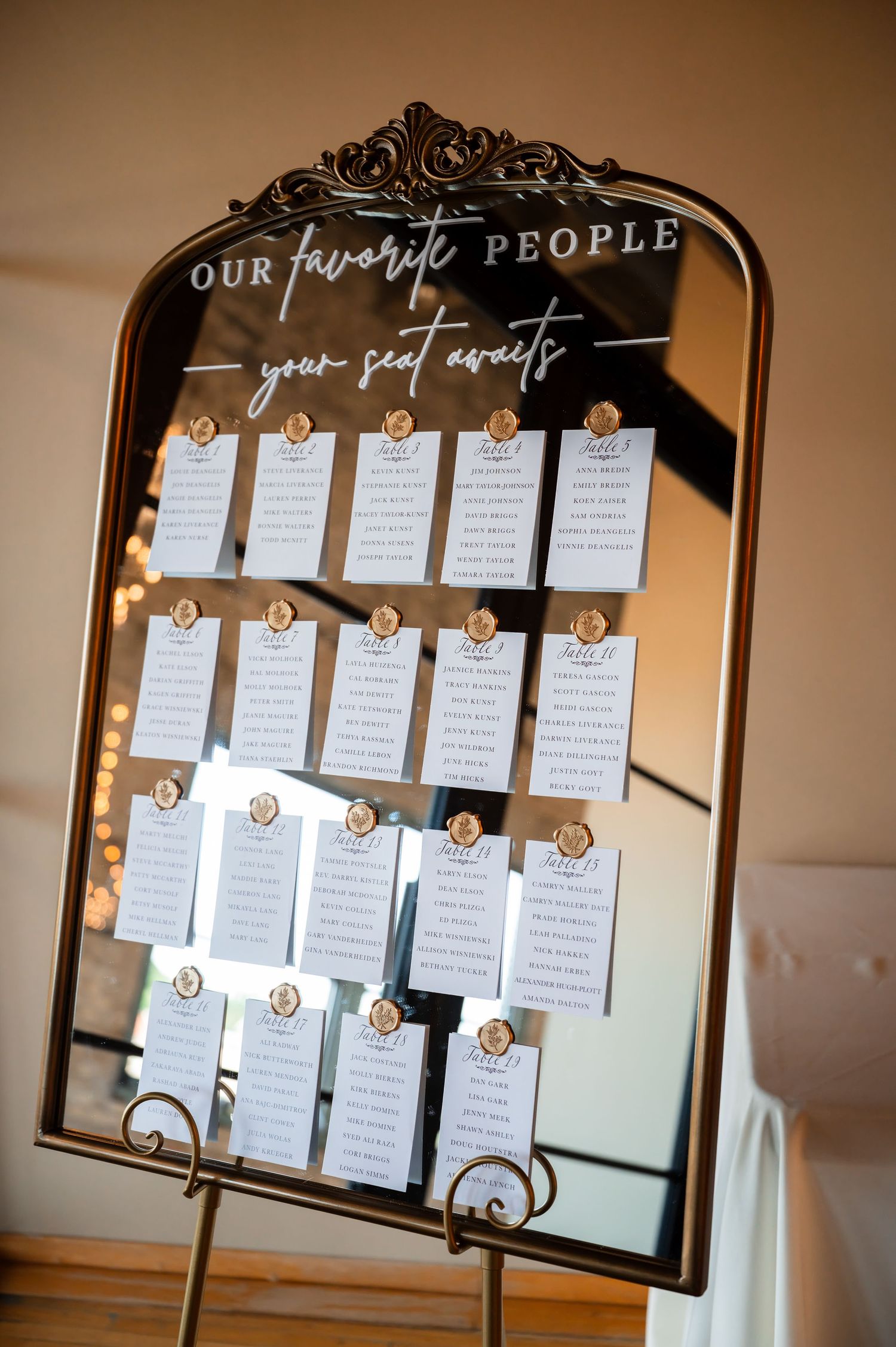 Elegant mirrored wedding seating chart display reading Our Favorite People with gold-accented table cards.