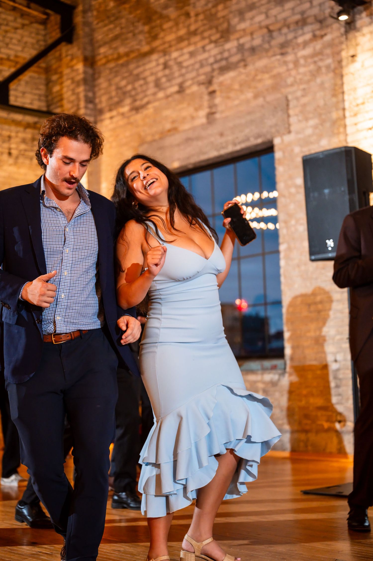 Guests dance energetically on the dance floor at a lively wedding reception in a brick venue.