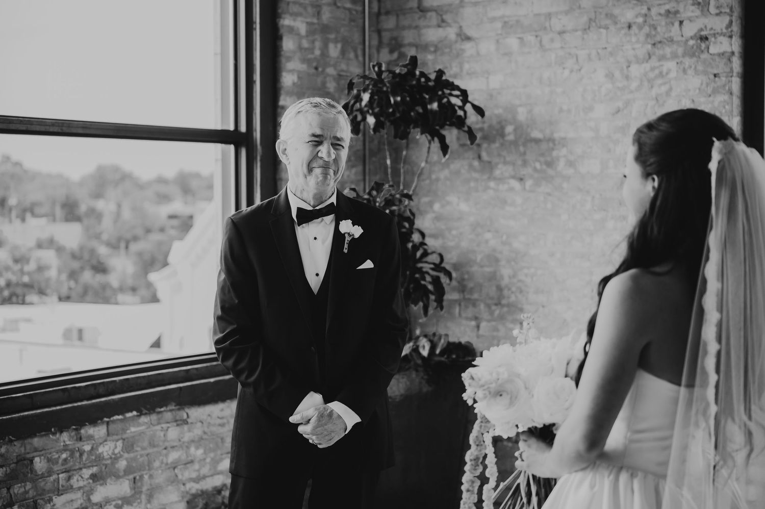 Emotional father seeing bride daughter for first time in wedding dress during first look moment.