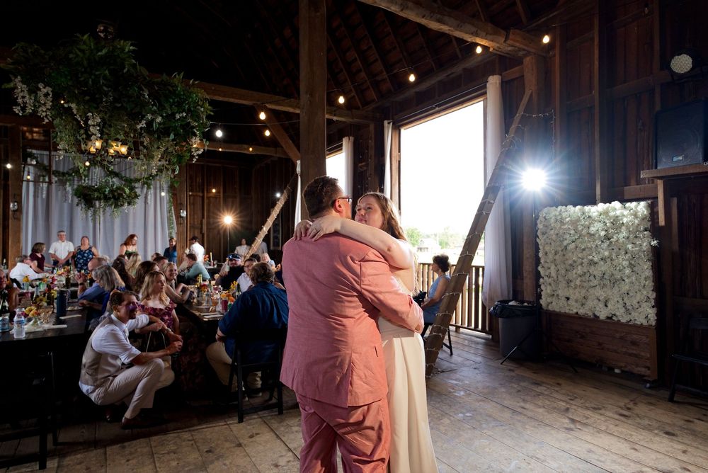 Bride and groom in a pink suit share their first dance during a rustic wedding reception at The Centennial Barn.