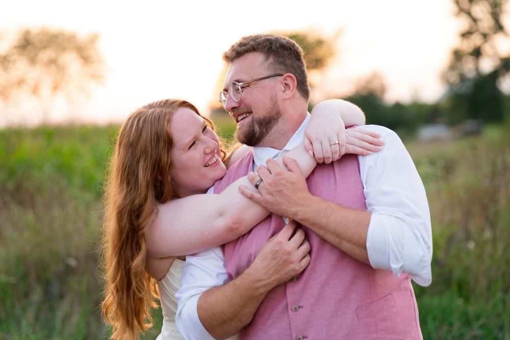 A bride and groom share a playful, laughing moment during golden hour couple portraits in an open field.