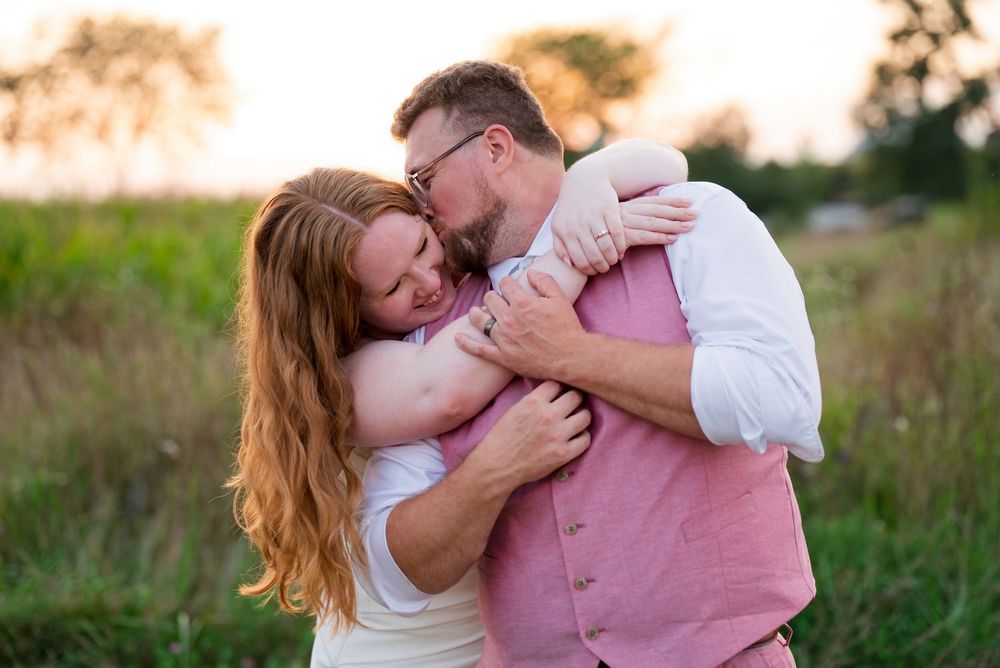 A bride and groom share a playful, cuddling moment during golden hour couple portraits in an open field.