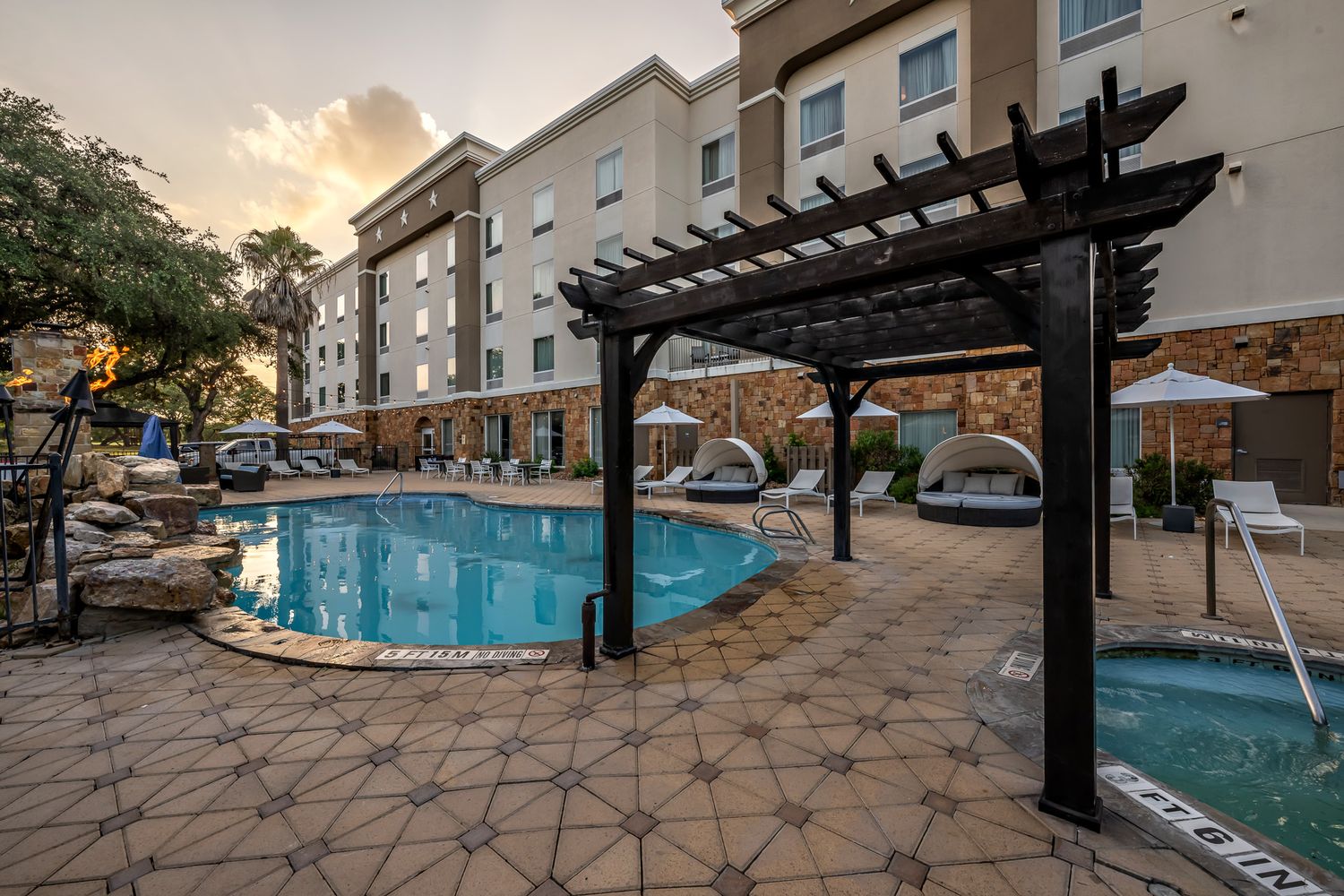 Outdoor hotel pool area with pergola, lounge chairs, and cabanas at sunset.