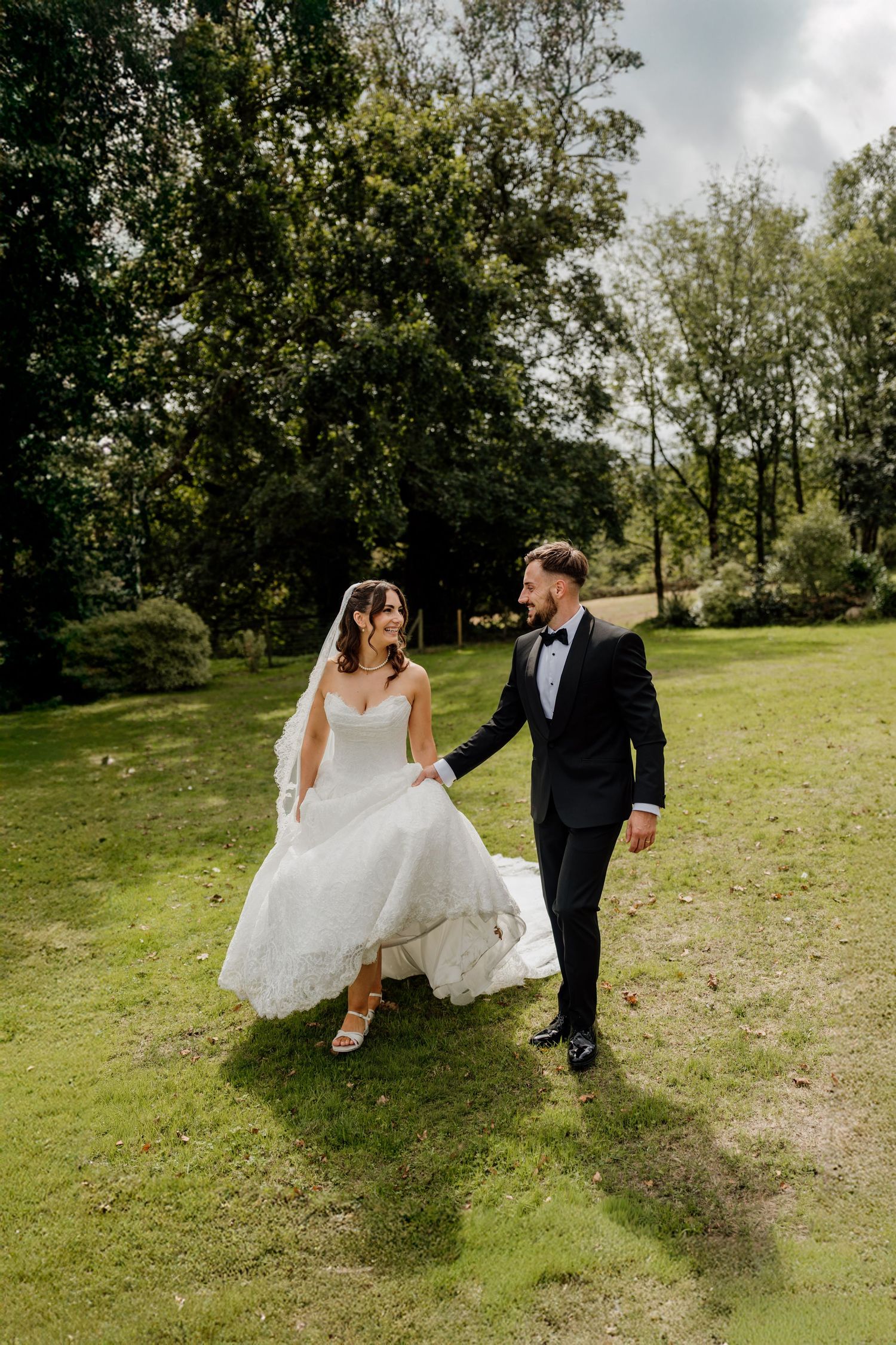 Bride and groom walk hand-in-hand through lush green park at The Green wedding venue in Liskeard.
