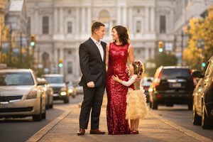 A couple and their young daughter pose elegantly on a city street with a grand building backdrop.