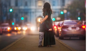 A woman and child embrace on a city sidewalk surrounded by colorful traffic lights at dusk.