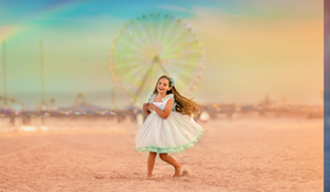 A joyful girl in a white dress twirls barefoot on a sandy beach with a ferris wheel behind her.