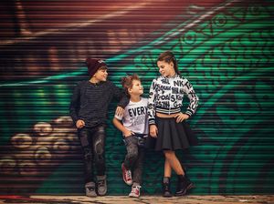 Three stylish kids pose confidently in front of a colorful graffiti wall.