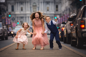 Three dressed-up children laugh and run joyfully down a city street together.
