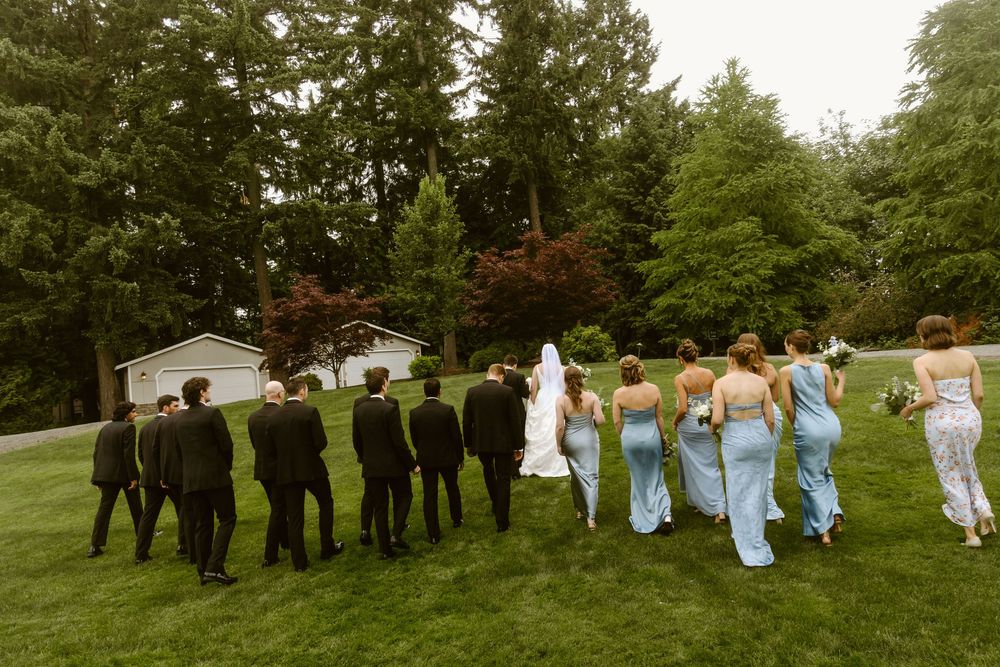 Wedding party walking away on green lawn, bride in white gown with bridesmaids in blue dresses.