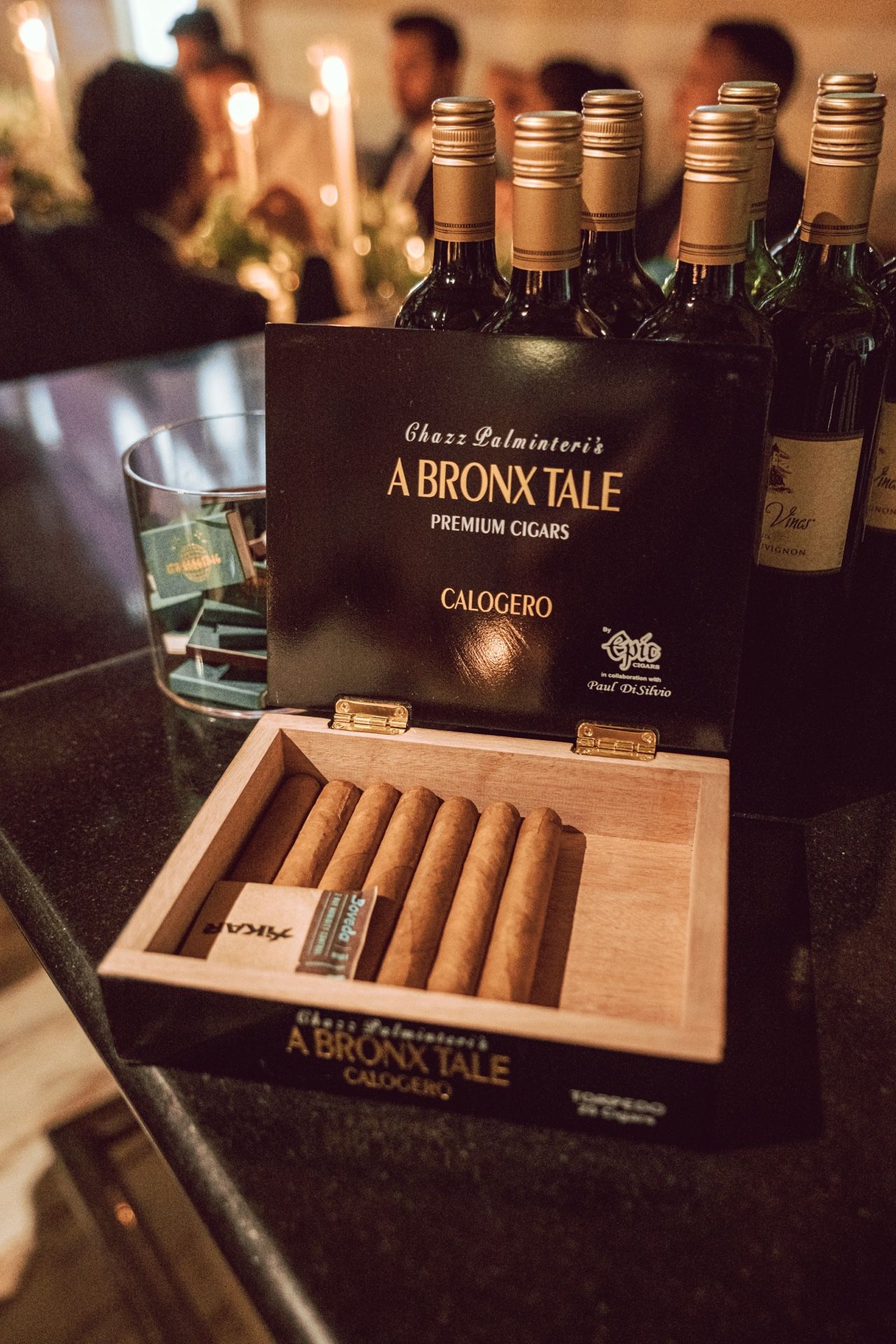 Open box of A Bronx Tale premium cigars by Chazz Palminteri displayed on table with wine bottles at elegant event.