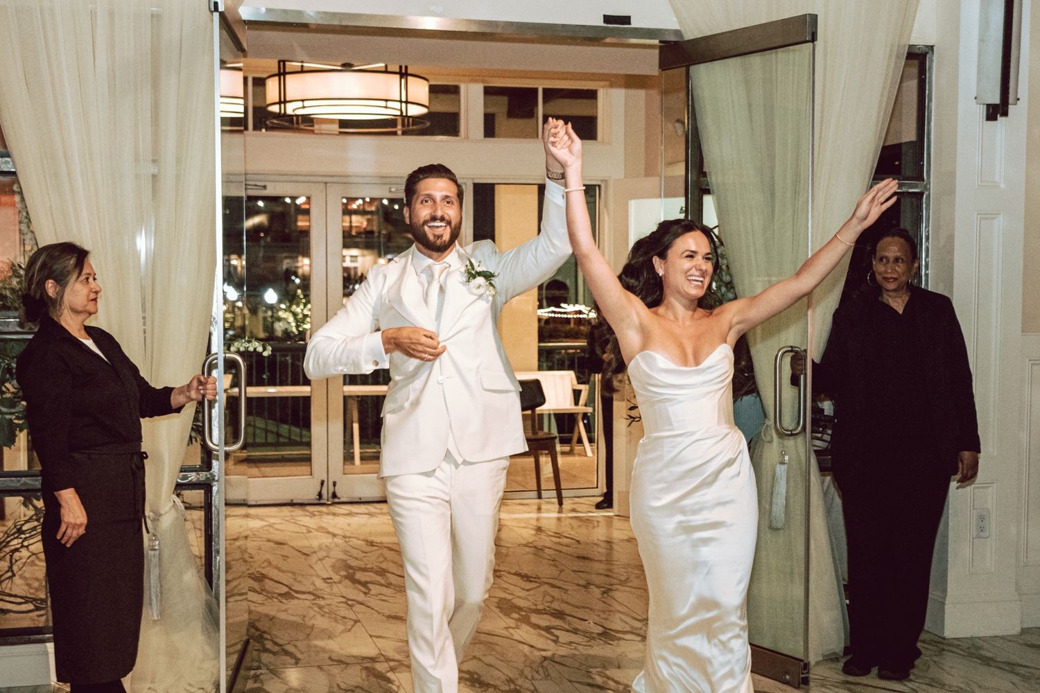Bride and groom make grand entrance at elegant wedding reception venue, arms raised in celebration.