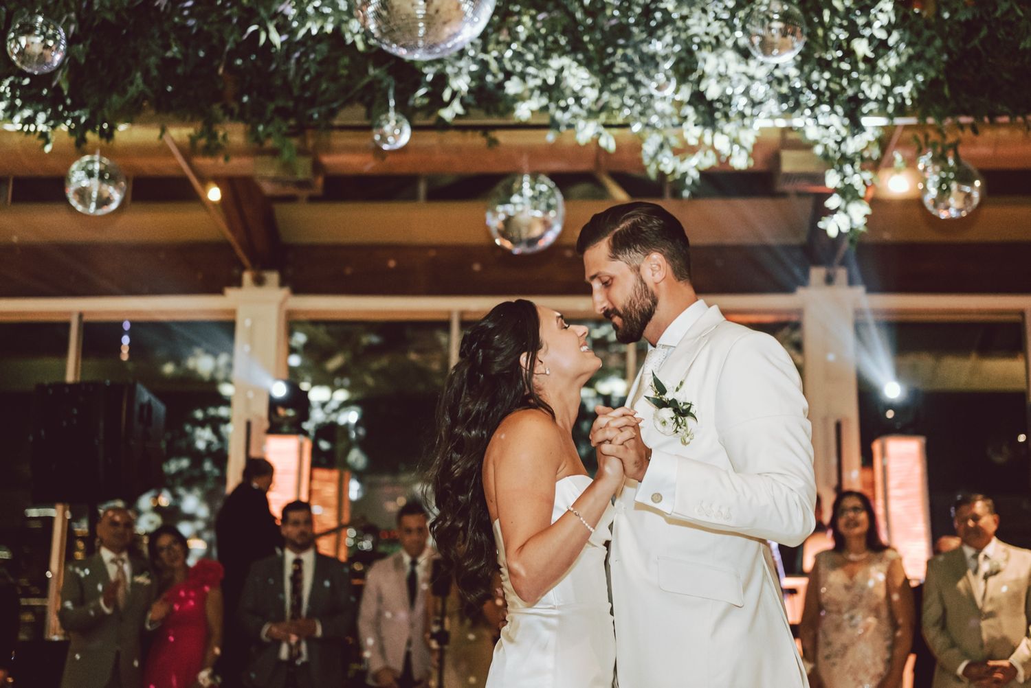 Bride and groom share first dance under hanging globe lights and floral greenery at elegant wedding reception.