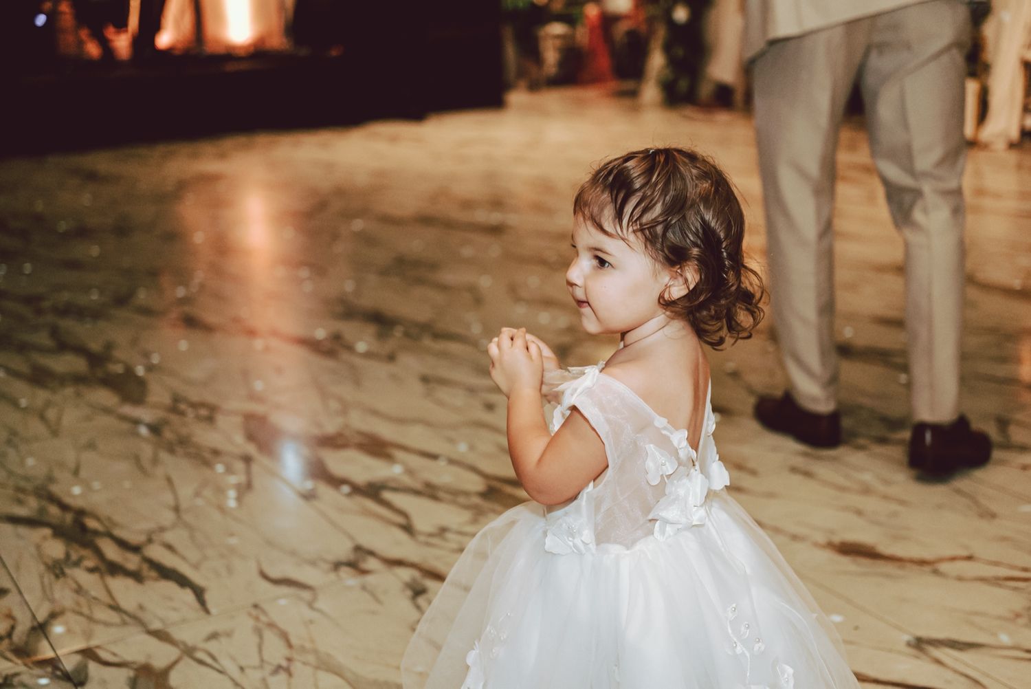 A little flower girl in a white tulle dress dances at an elegant wedding reception.