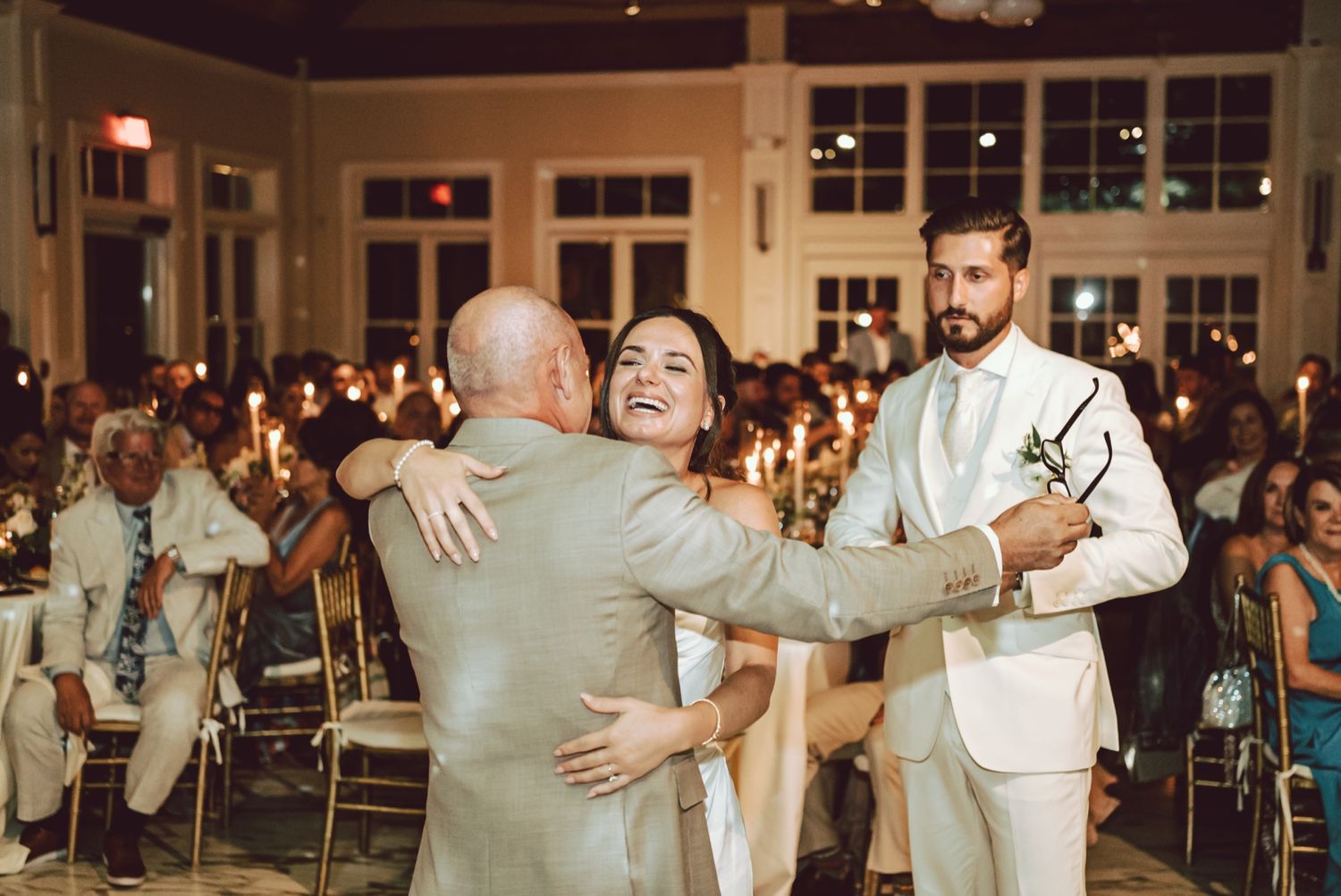 Bride and groom embrace guests during candlelit wedding reception celebration.