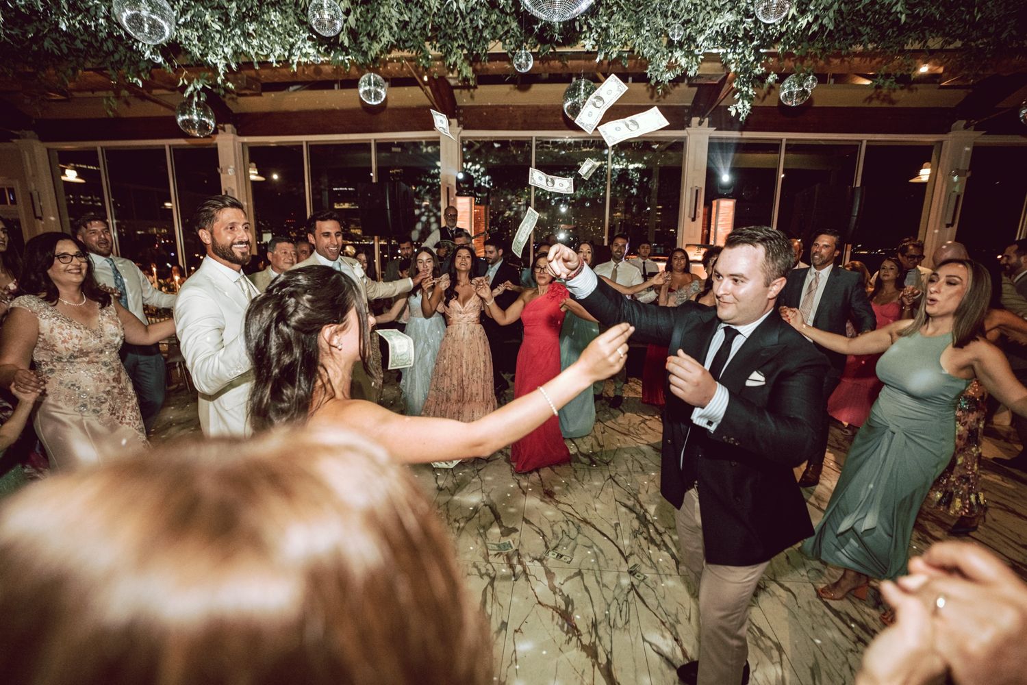 Bride and groom dancing with guests at a lively wedding reception party indoors with elegant decor.
