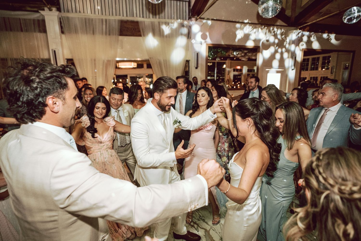 Bride and groom share first dance surrounded by cheering wedding guests in elegant venue.