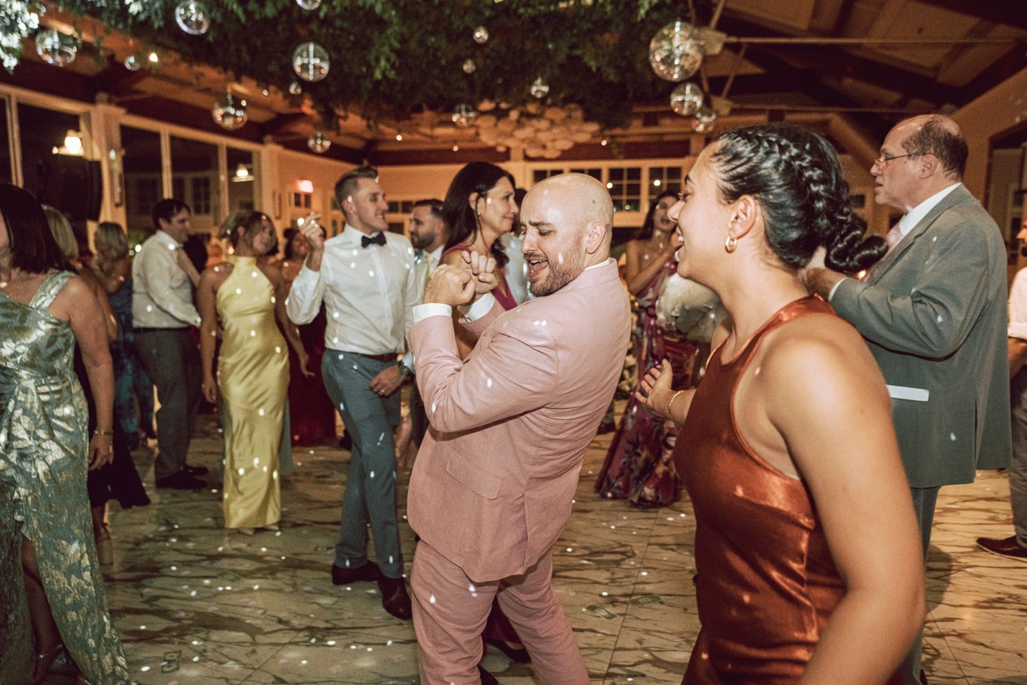 Guests dancing joyfully at an elegant indoor wedding reception with disco ball lighting and festive decor.