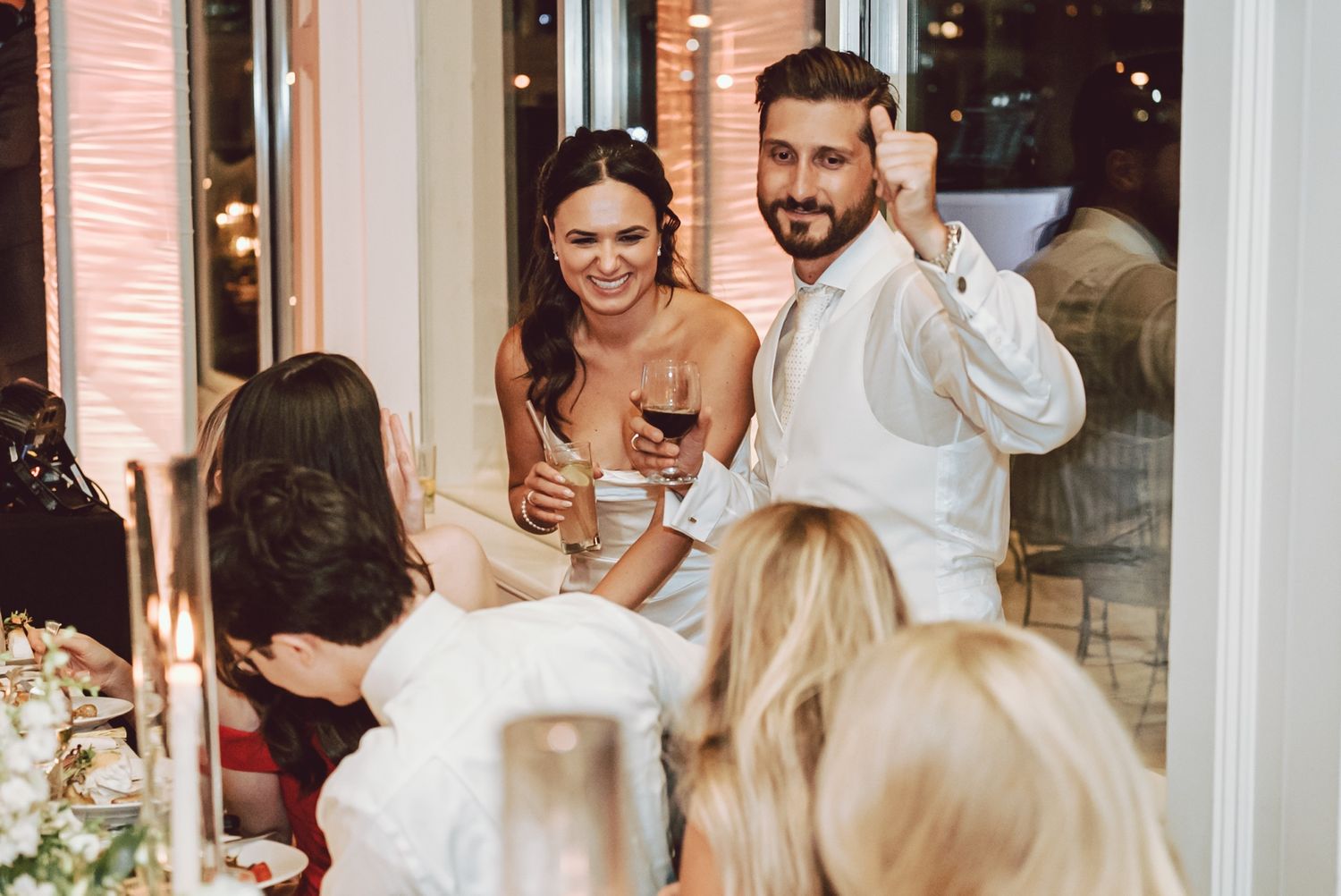 Bride and groom laughing with guests at candlelit wedding reception dinner table.